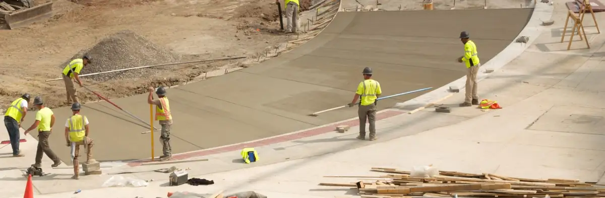 Commercial concrete flatwork crew bull-floating and screeding a curved drive lane beside a curb