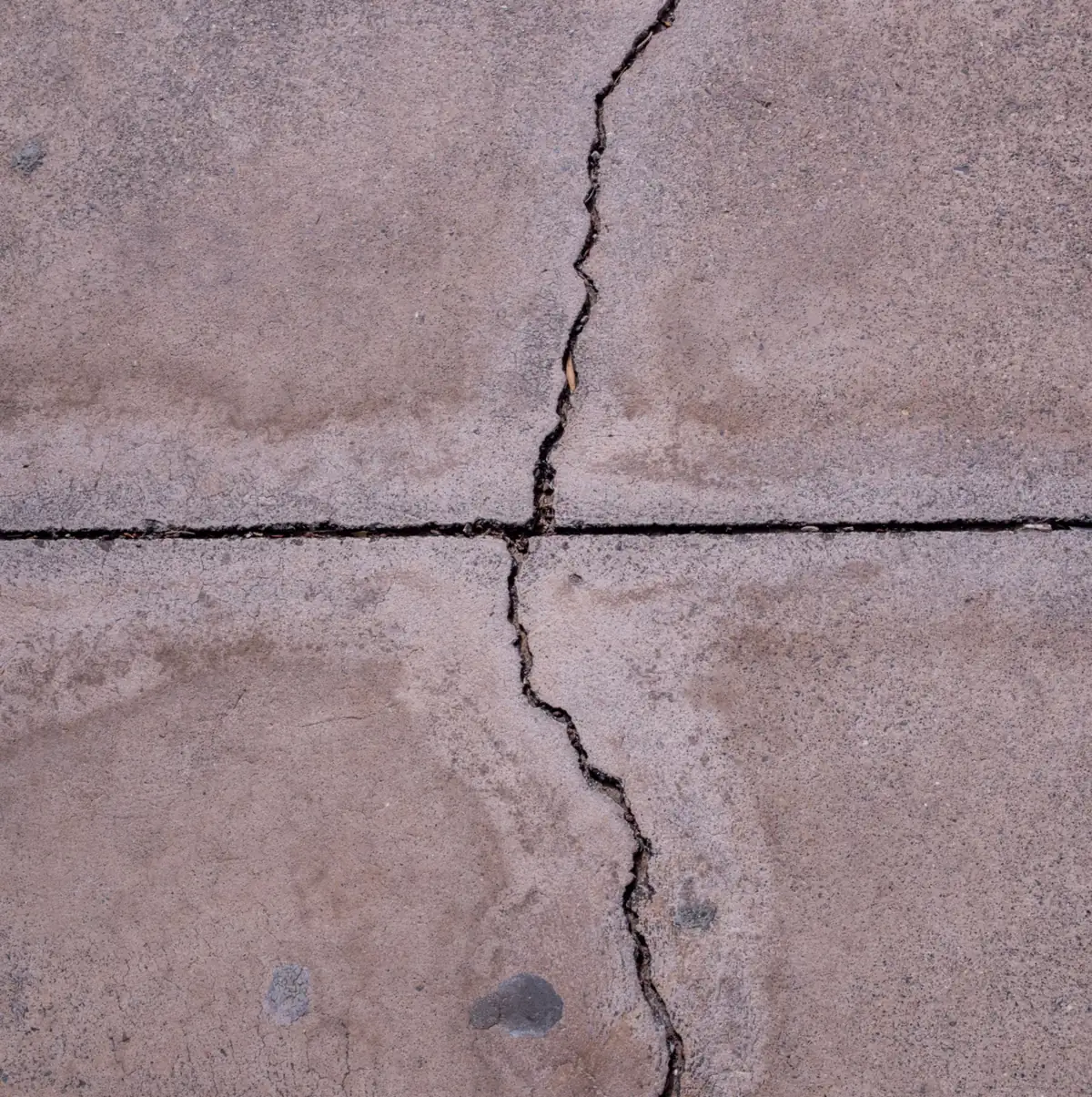 a wide crack running across a sawn control joint in a weathered slab.