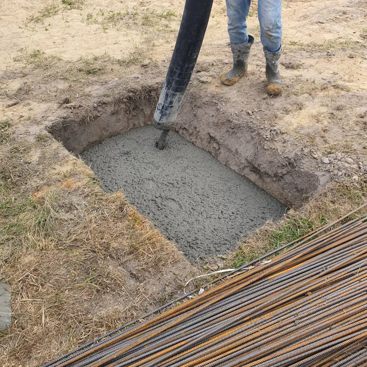 Pump hose filling an excavated concrete footing trench as a worker guides the pour