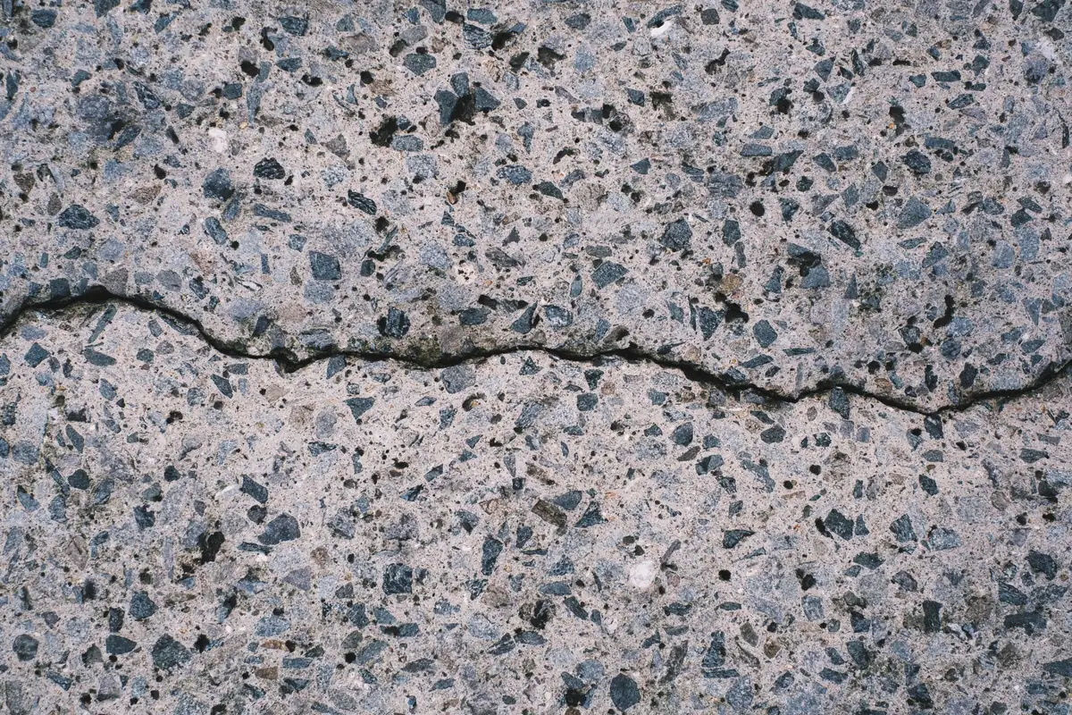 a hairline crack through a concrete surface with dark aggregate showing.