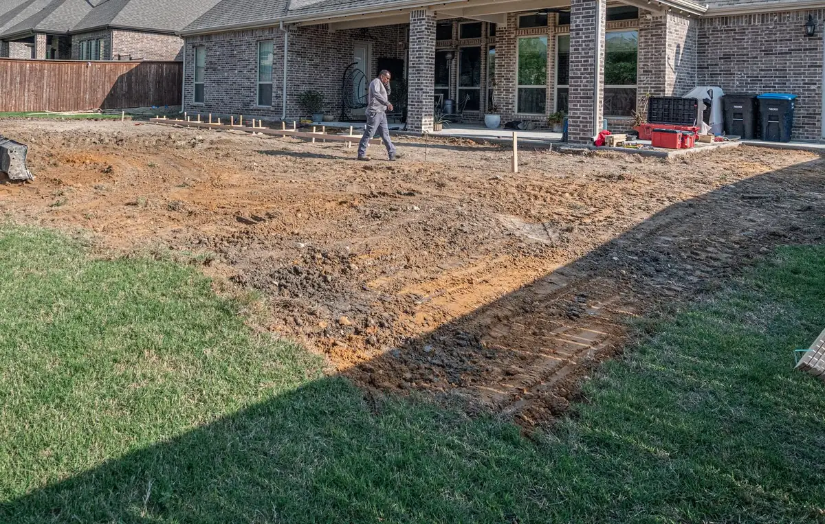 Backyard stripped to subgrade with form stakes set for a new concrete patio