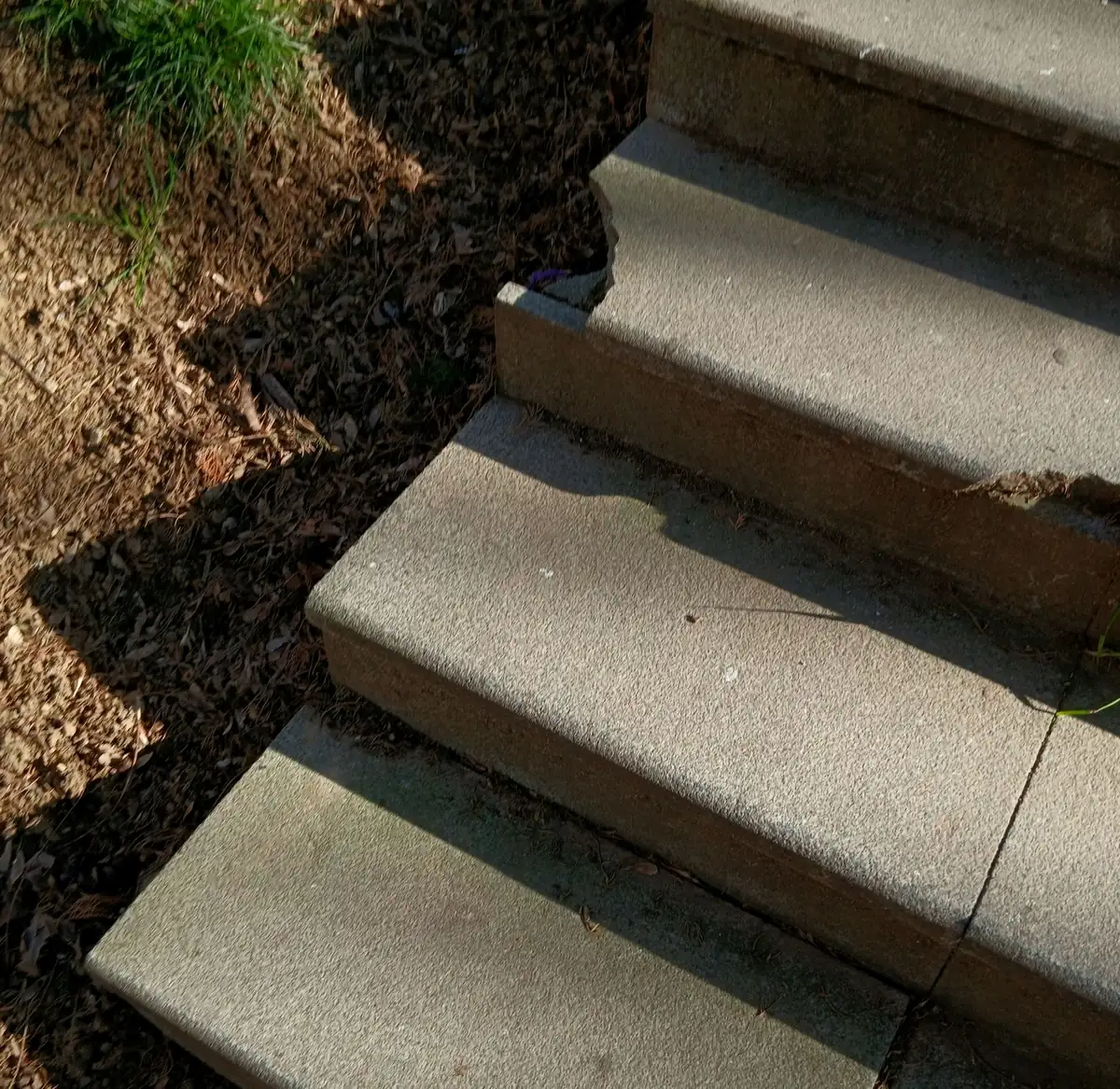 Outdoor concrete steps with chipped and broken nosings on two treads